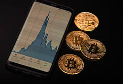 Symbolische Bitcoin-Münzen und der dazugehörige Kursverlauf auf dem Bildschirm eines Smartphones.