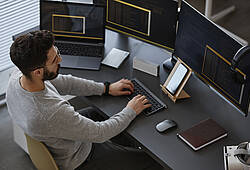 Symbolfoto: Ein Mann sitzt in einem Büro vor einem PC mit mehreren Bildschirmen.