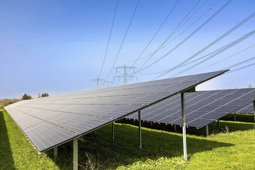 Das Bild zeigt eine Photovoltaik-Anlage mit Strommasten im Hintergrund in Bayern.