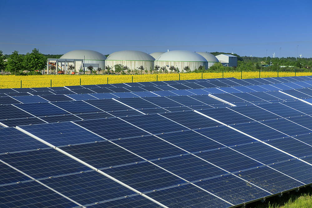 Das Bild zeigt eine Biogas-Anlage und ein blühendes Rapsfeld im Hintergrund und eine Photovoltaik-Anlage im Vordergrund.