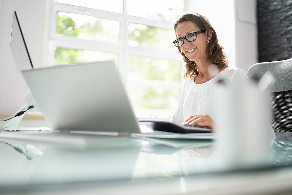 Eine Frau sitzt in einem hellen Büro am Schreibtisch vor einem Laptop.